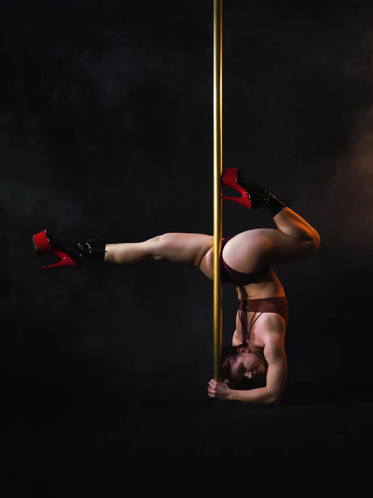 Dansatoare în pantofi roșii cu platformă, în stând pe umăr lângă bară